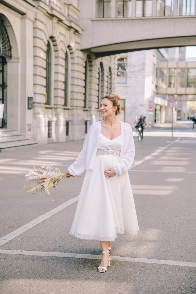 Schwangere Braut mit Brautstrauss und einem Kleid von piqyourdress, erhältlich bei Zauberbraut Zürich